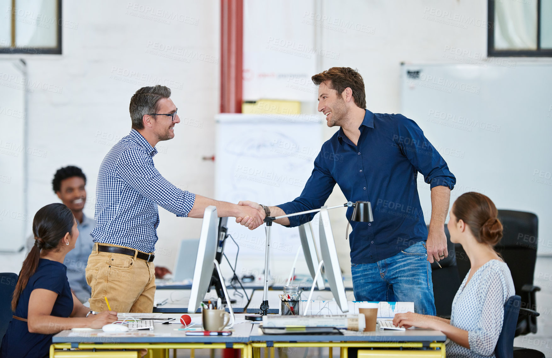 Buy stock photo Shot of two designers shaking hands over their computers in an office