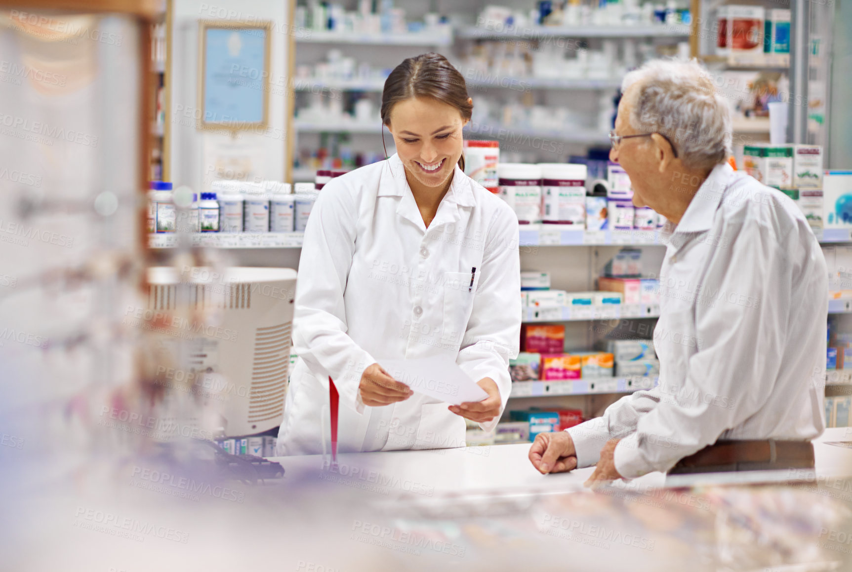 Buy stock photo Shot of a young pharmacist helping an elderly customer at the prescription counter