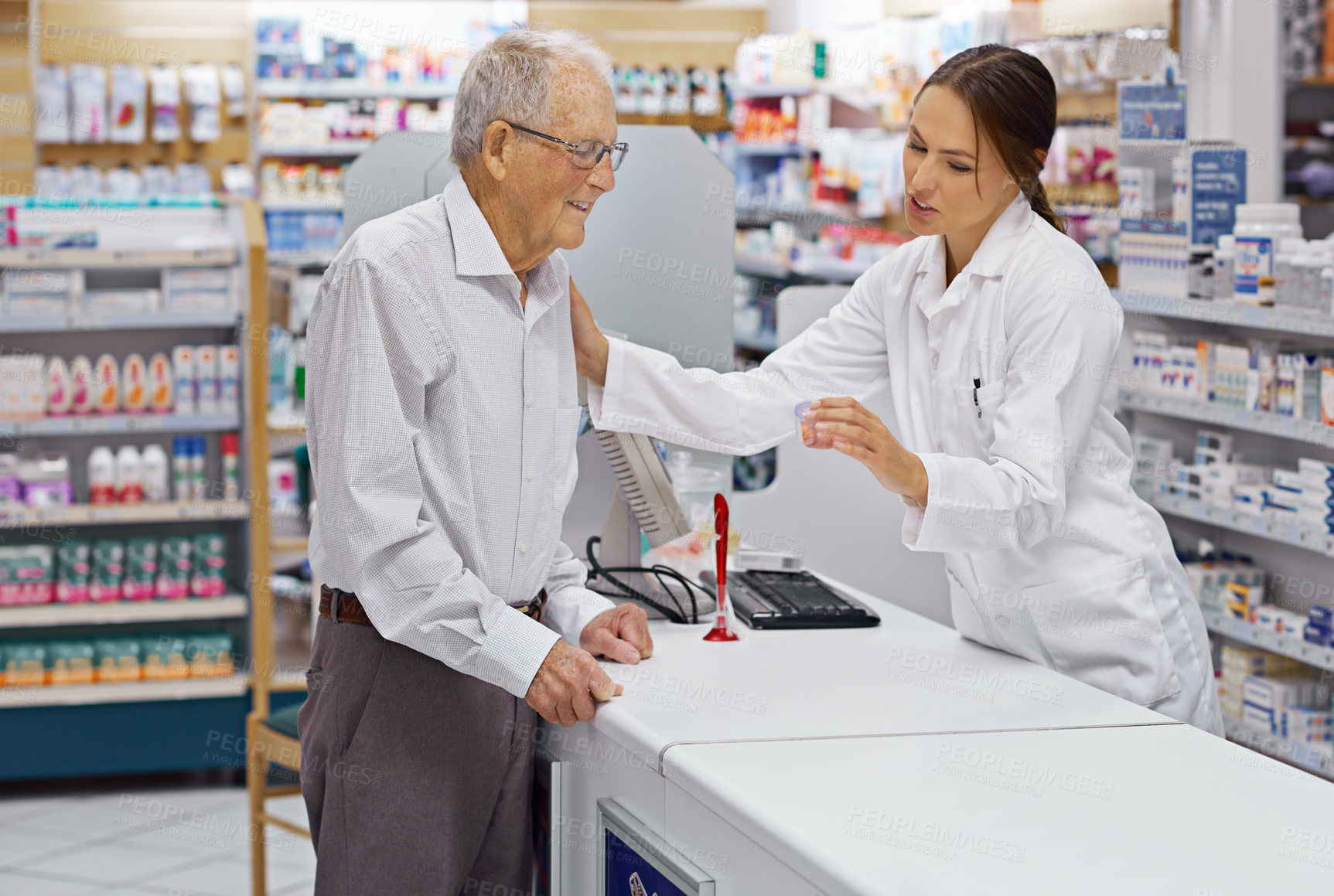 Buy stock photo Shot of a young pharmacist helping an elderly customer at the prescription counter