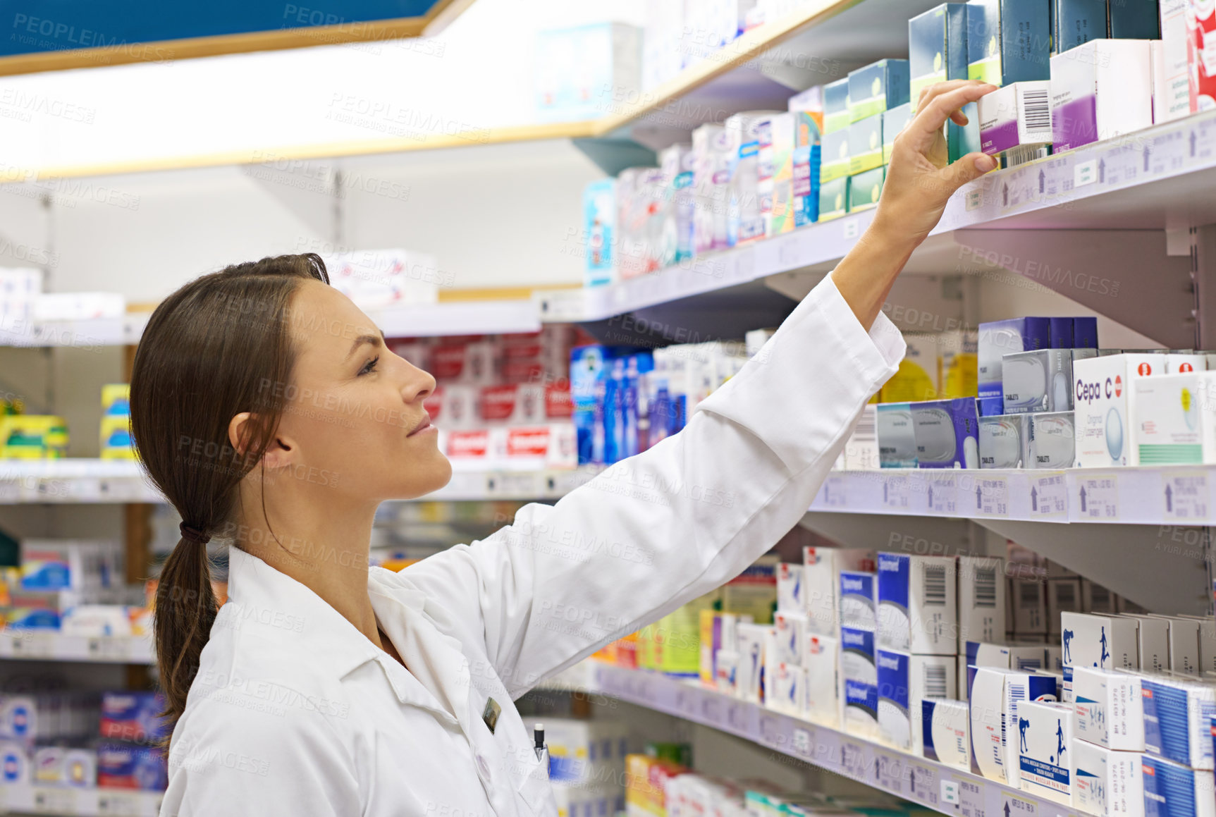Buy stock photo Shot of an attractive young pharmacist checking stock in an aisle