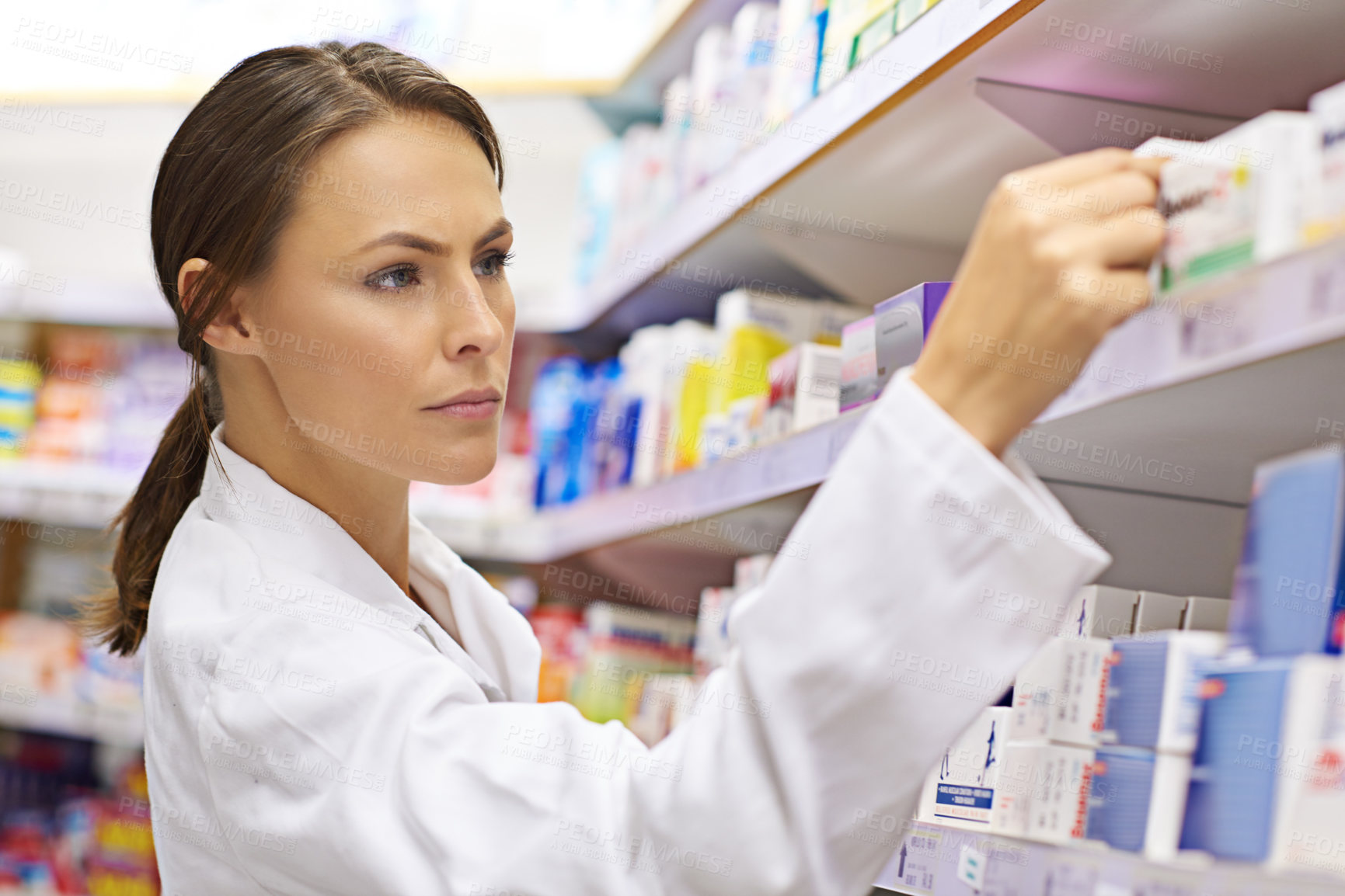 Buy stock photo Shot of an attractive young pharmacist checking stock in an aisle