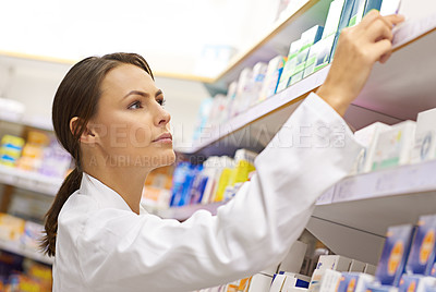 Buy stock photo Shot of an attractive young pharmacist checking stock in an aisle