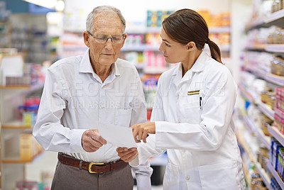 Buy stock photo Shot of a young pharmacist helping an elderly customer with his prescription