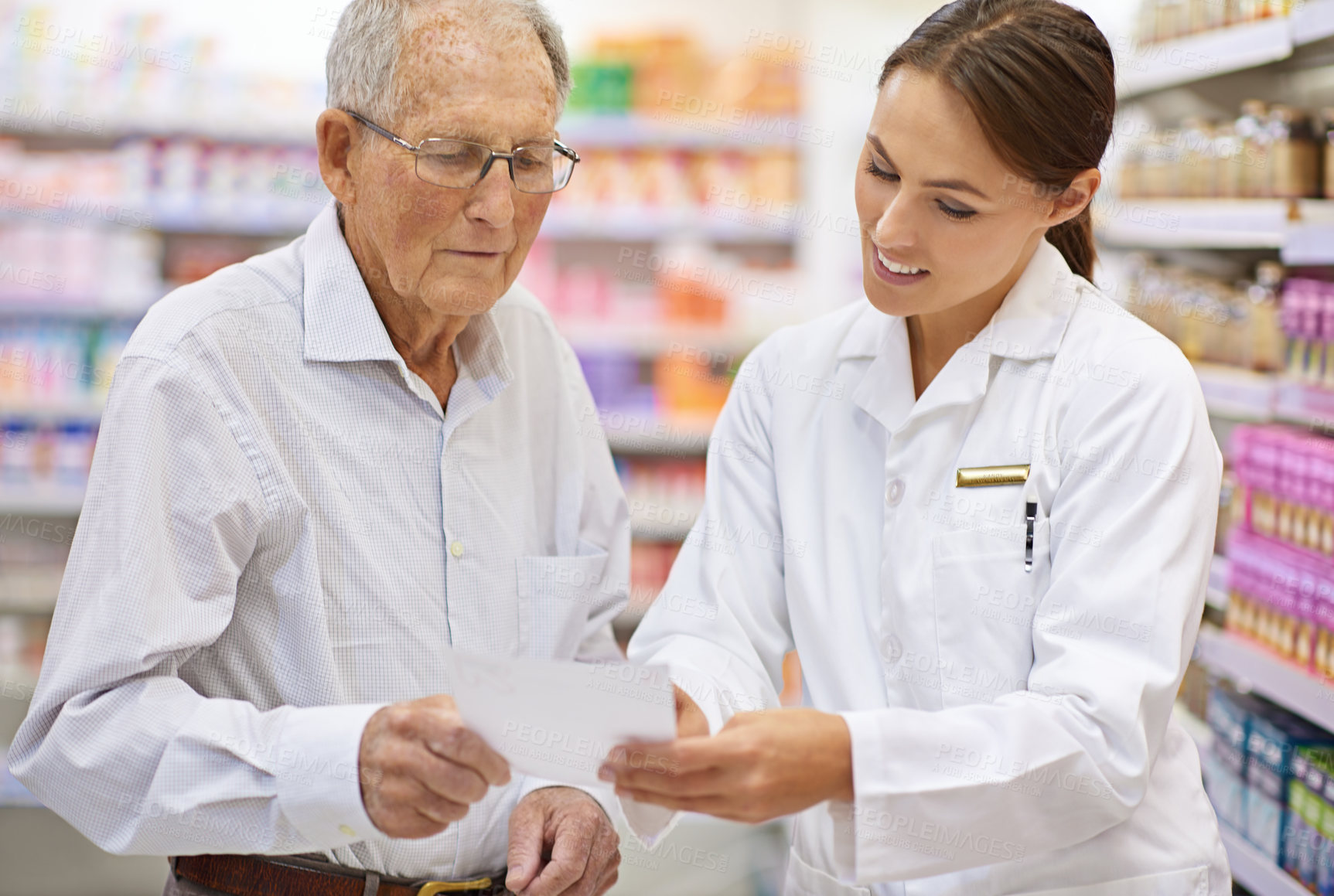 Buy stock photo Shot of a young pharmacist helping an elderly customer with his prescription