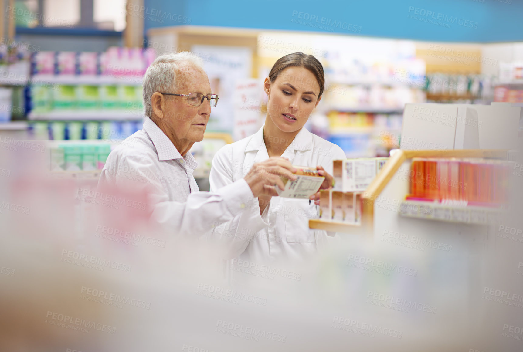 Buy stock photo Shot of a young pharmacist helping an elderly customer