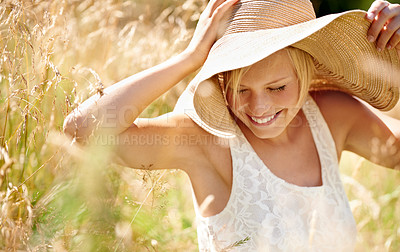 Buy stock photo Shot of a beautiful young woman in a sunhat walking through tall grass