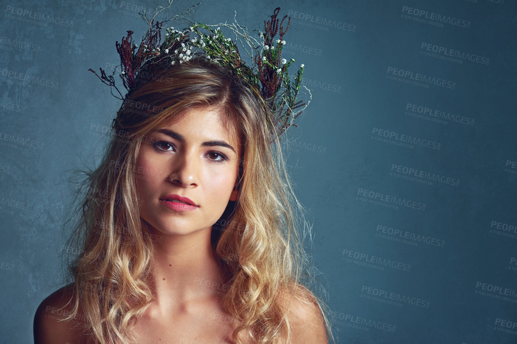 Buy stock photo Cropped shot of a young woman posing with flowers in her hair against a blue background