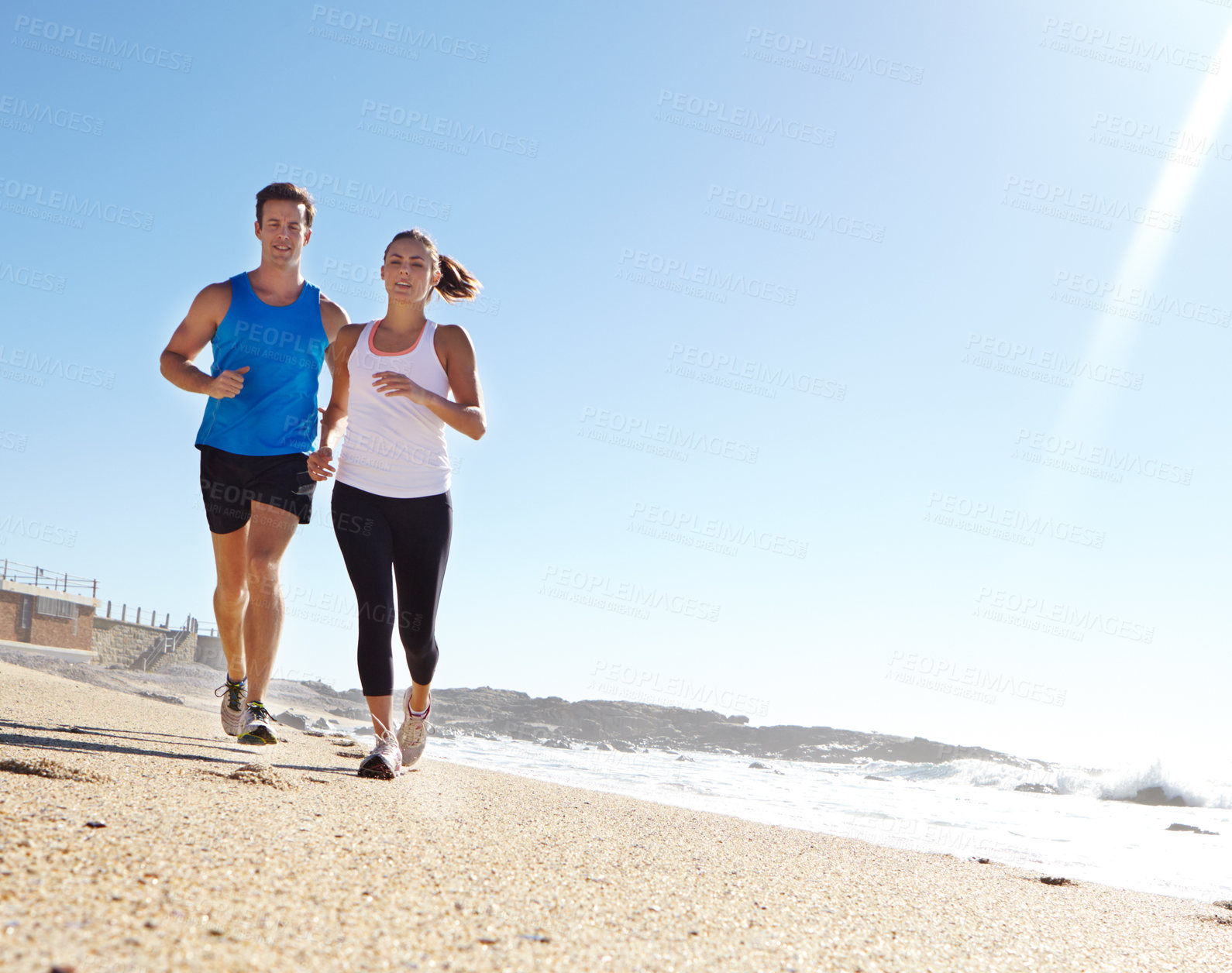 Buy stock photo Shot of a young couple jogging together by the beach