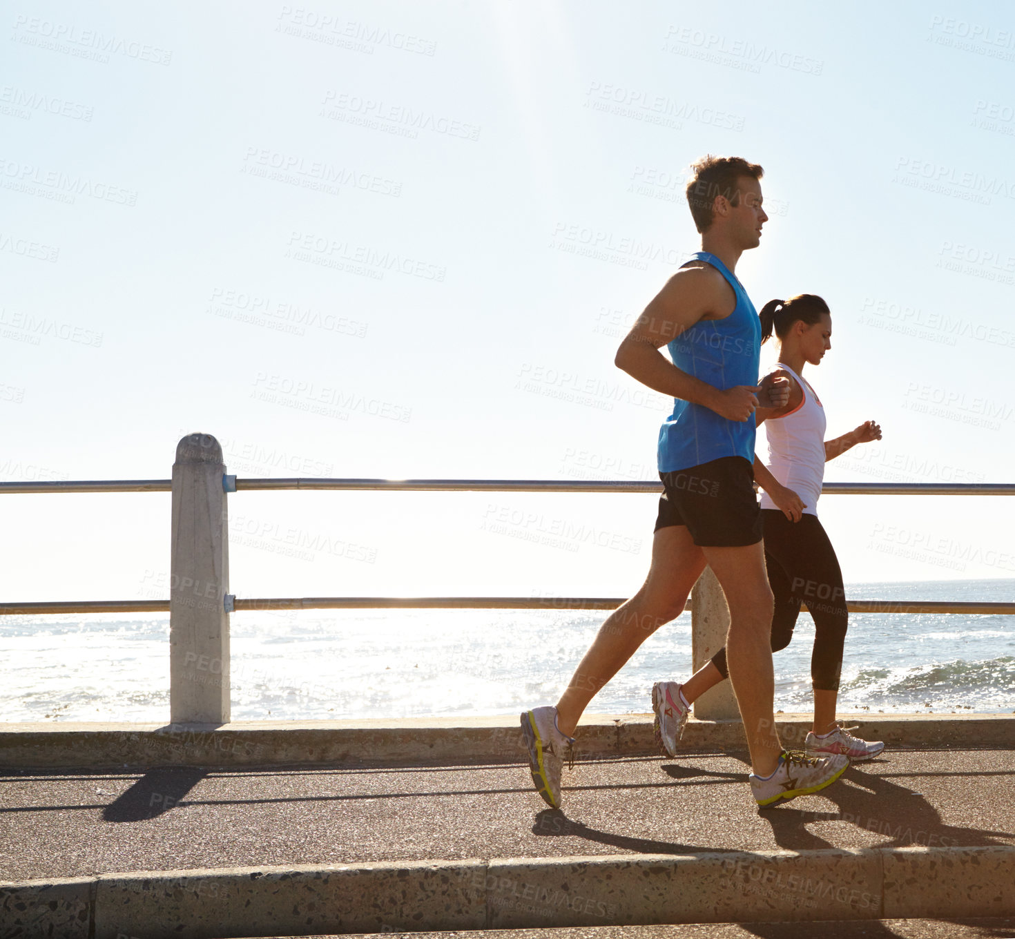 Buy stock photo Shot of a young couple jogging together on the promenade 