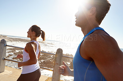 Buy stock photo Shot of a young couple jogging together on the promenade 