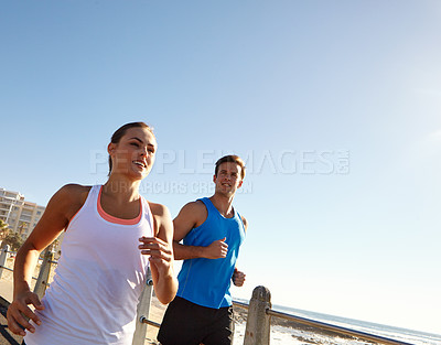 Buy stock photo Shot of a young couple jogging together on the promenade 