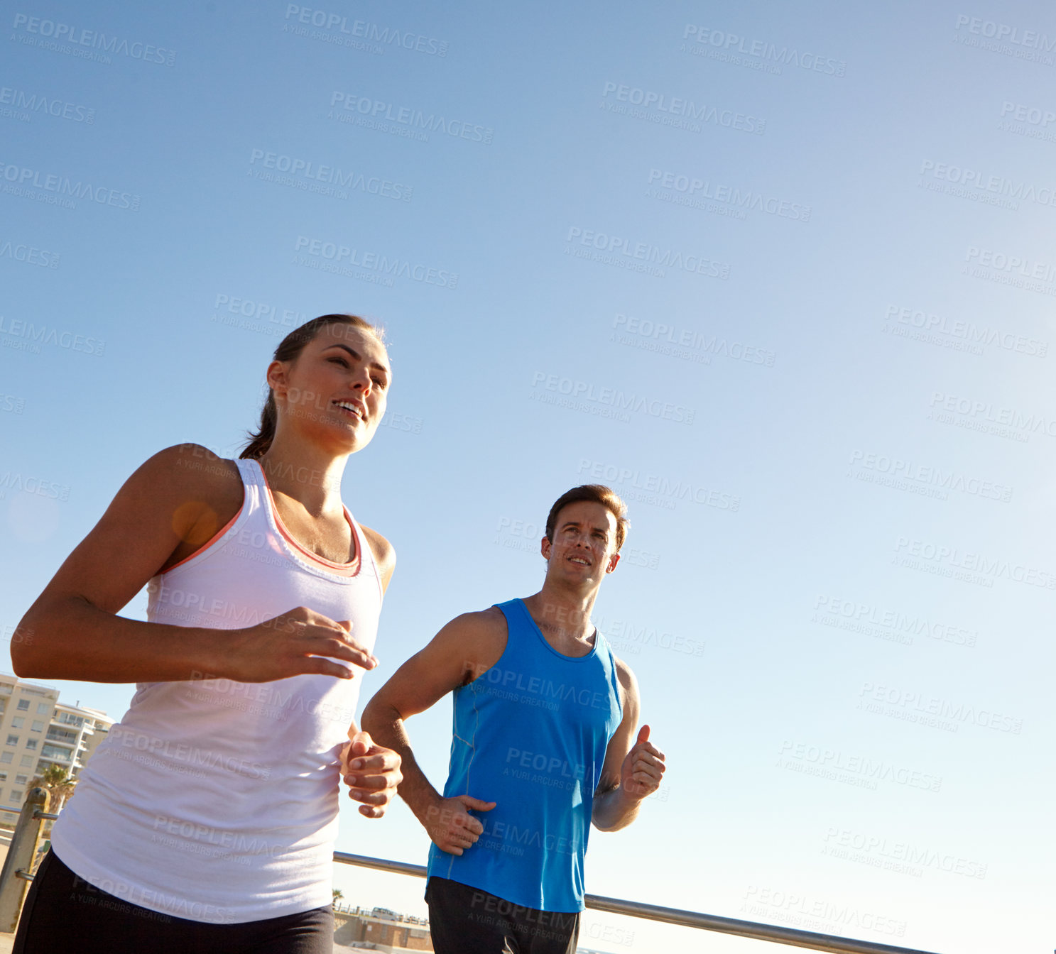 Buy stock photo Shot of a young couple jogging together on the promenade 