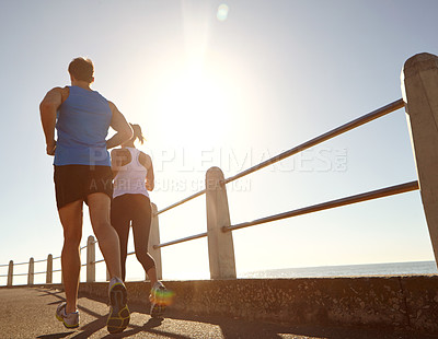 Buy stock photo Rearview shot of a young couple jogging together the promenade 