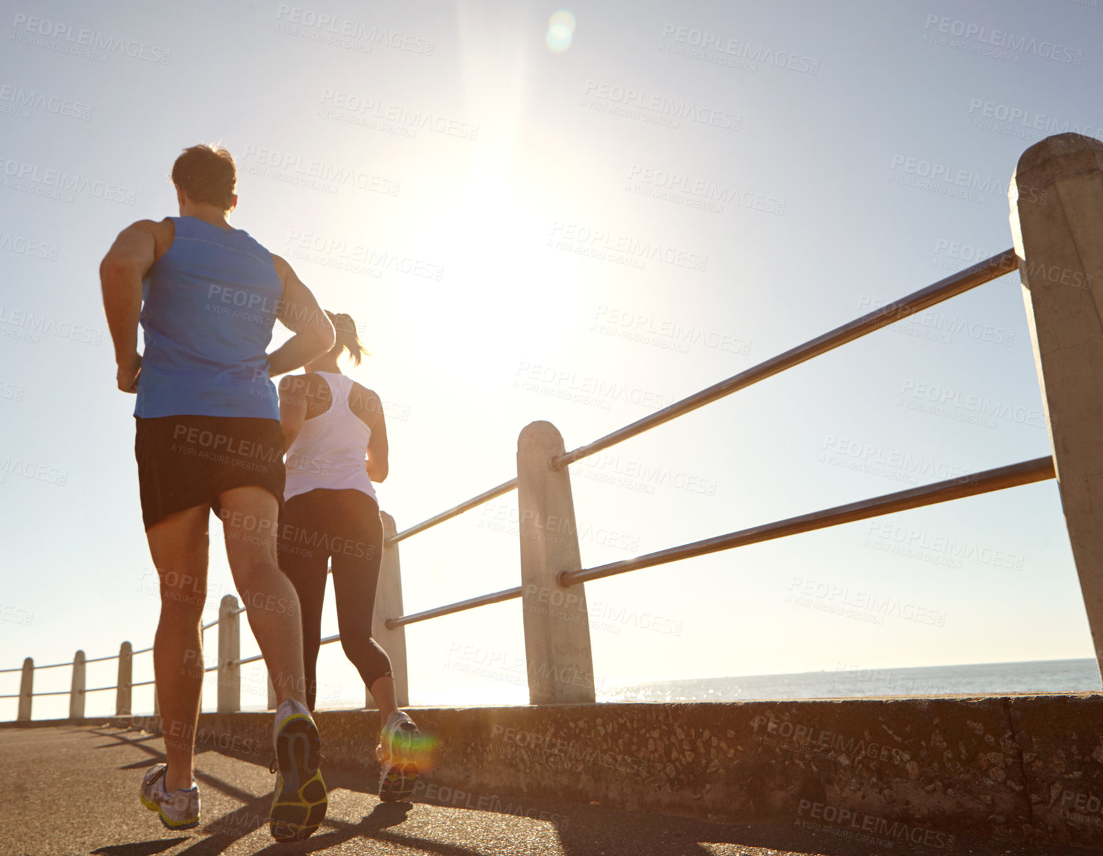 Buy stock photo Rearview shot of a young couple jogging together the promenade 