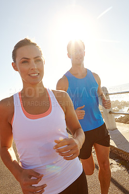 Buy stock photo Shot of a young couple jogging together on the promenade 