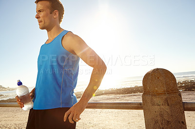 Buy stock photo Shot of a man holding a bottle of water and taking a break after a long jog 