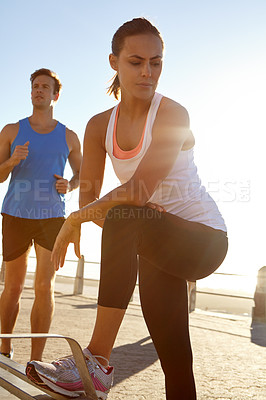 Buy stock photo Shot of a woman in sportswear taking a break after a jog with a man in the background