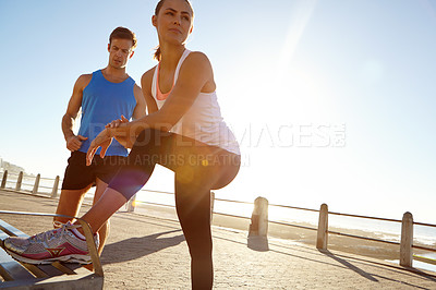Buy stock photo Shot of a woman stretching against a bench with a man standing in the background