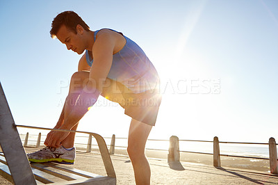 Buy stock photo Shot of an athletic man tying his shoe laces on a bench 