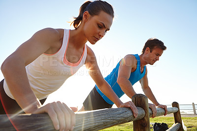 Buy stock photo A young couple doing push ups against a wooden fence