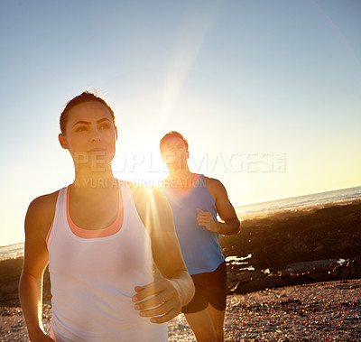 Buy stock photo Shot of a young couple jogging together by the beach