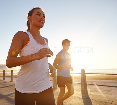 Buy stock photo Shot of two people jogging on the promenade