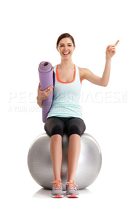 Buy stock photo Shot of a young woman pointing at something in a studio with her yoga mat and exercise ball