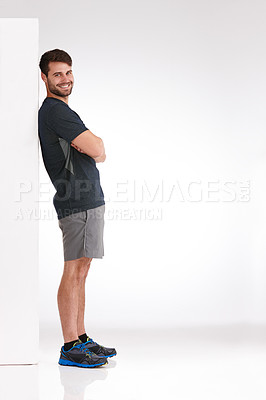 Buy stock photo Studio shot of a smiling young man leaning casually against a blank billboard