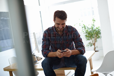 Buy stock photo Shot of a casual young designer sending a text on his phone in his office