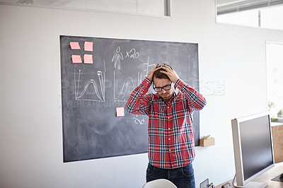 Buy stock photo Shot of a frustrated young designer in his office, holding his head in his hands