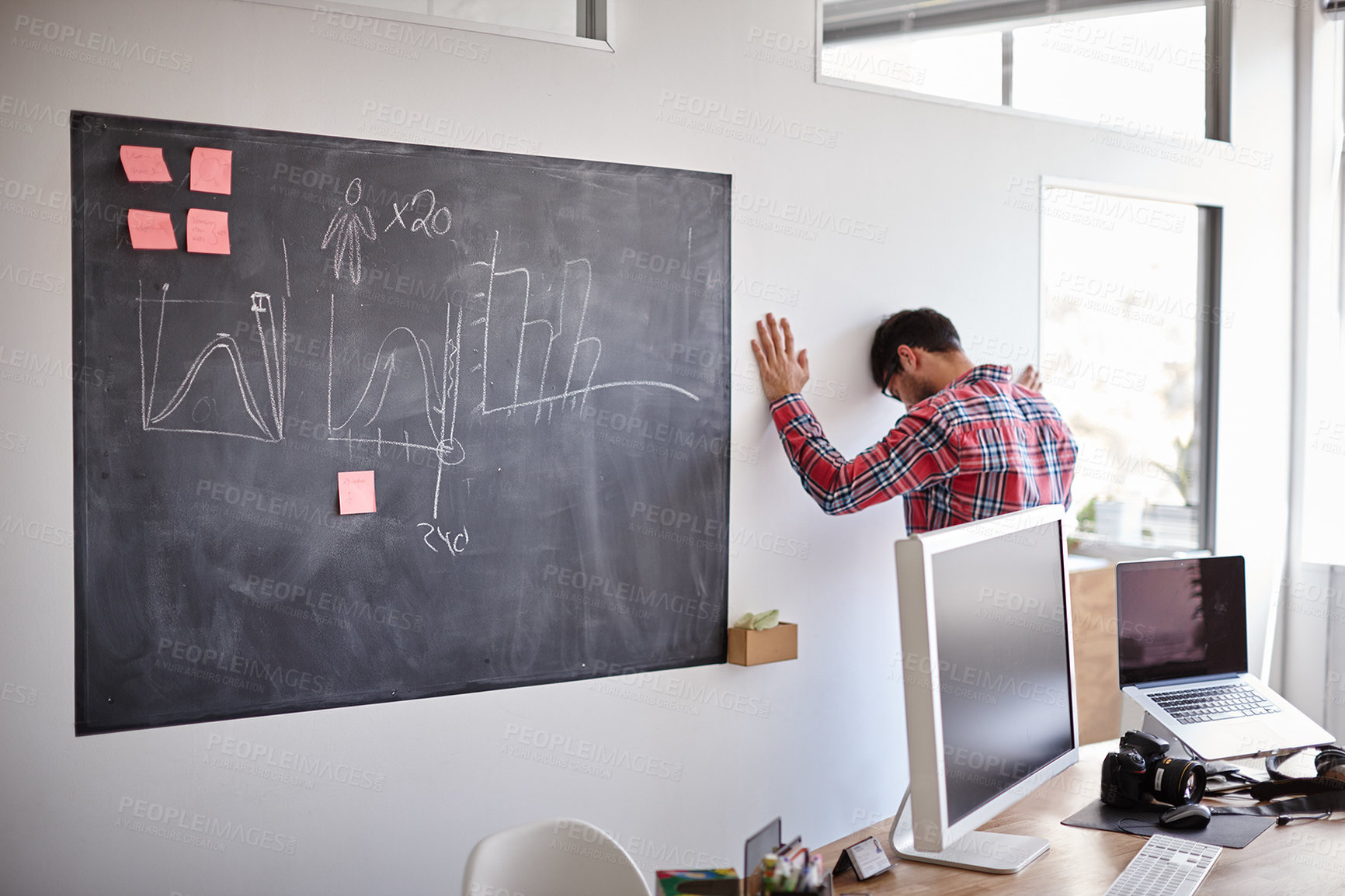 Buy stock photo Shot of a desperate young designer with his head against the wall in his office