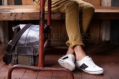 Buy stock photo Person, legs, and sneaker on bench with bag for fashion, aesthetic and trendy for comfort and travel outdoor. Pants, shoes and leather case on break or holiday for hipster clothes, relax and sitting