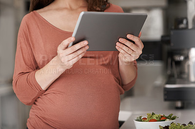 Buy stock photo Cropped shot of a pregnant woman using her tablet while eating a salad in the kitchen