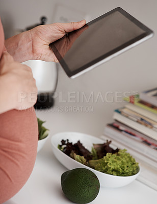 Buy stock photo Cropped shot of a pregnant woman using her tablet while eating a salad in the kitchen