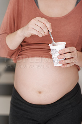 Buy stock photo Cropped shot of a young pregnant woman eating a yogurt in the kitchen