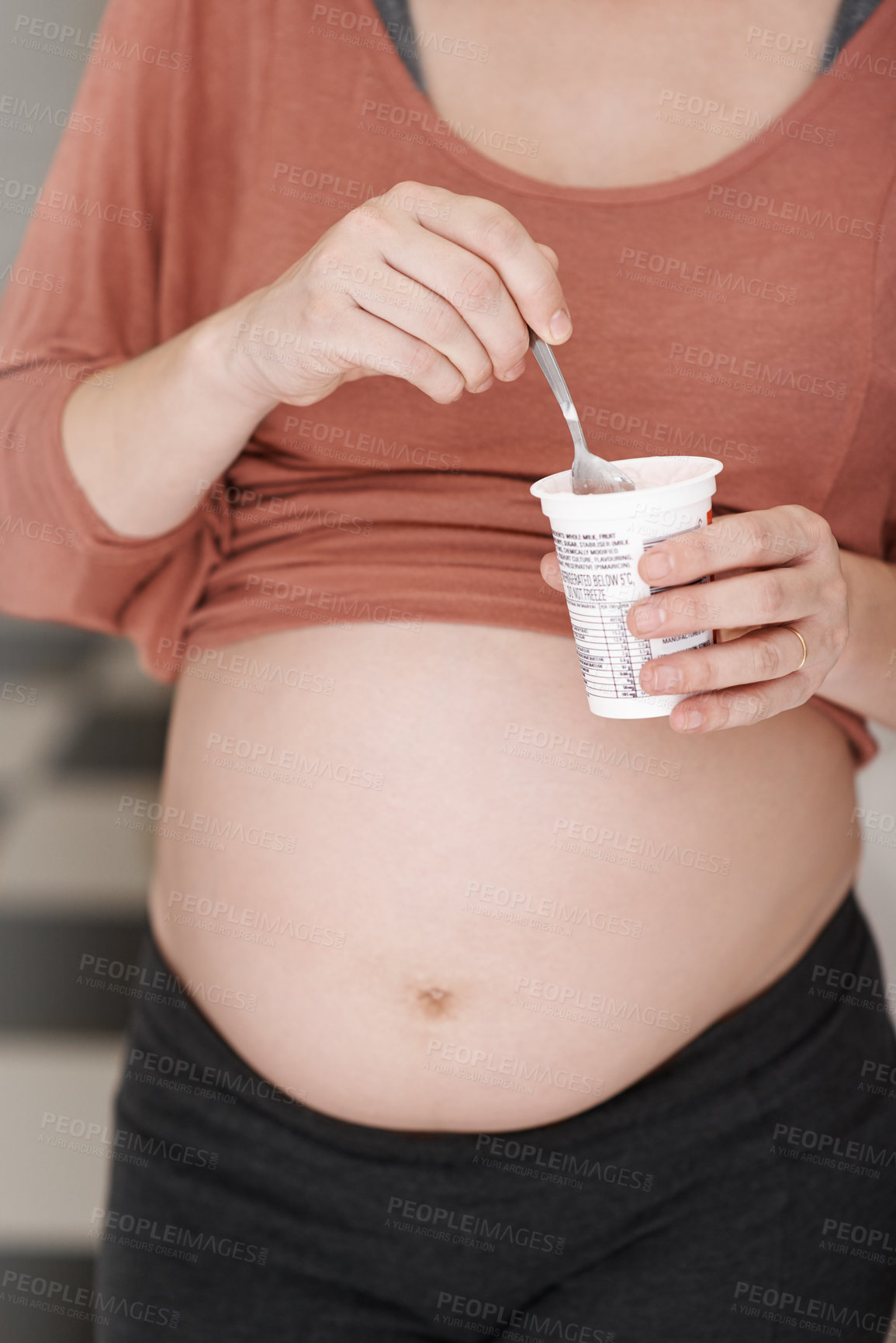 Buy stock photo Cropped shot of a young pregnant woman eating a yogurt in the kitchen