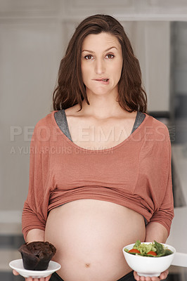 Buy stock photo Cropped portrait of a young pregnant woman deciding between a salad or a cupcake in the kitchen