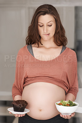 Buy stock photo Cropped shot of a young pregnant woman deciding between a salad or a cupcake in the kitchen