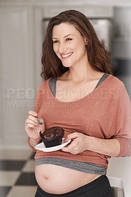 Buy stock photo Cropped shot of a young pregnant woman eating a cupcake in the kitchen