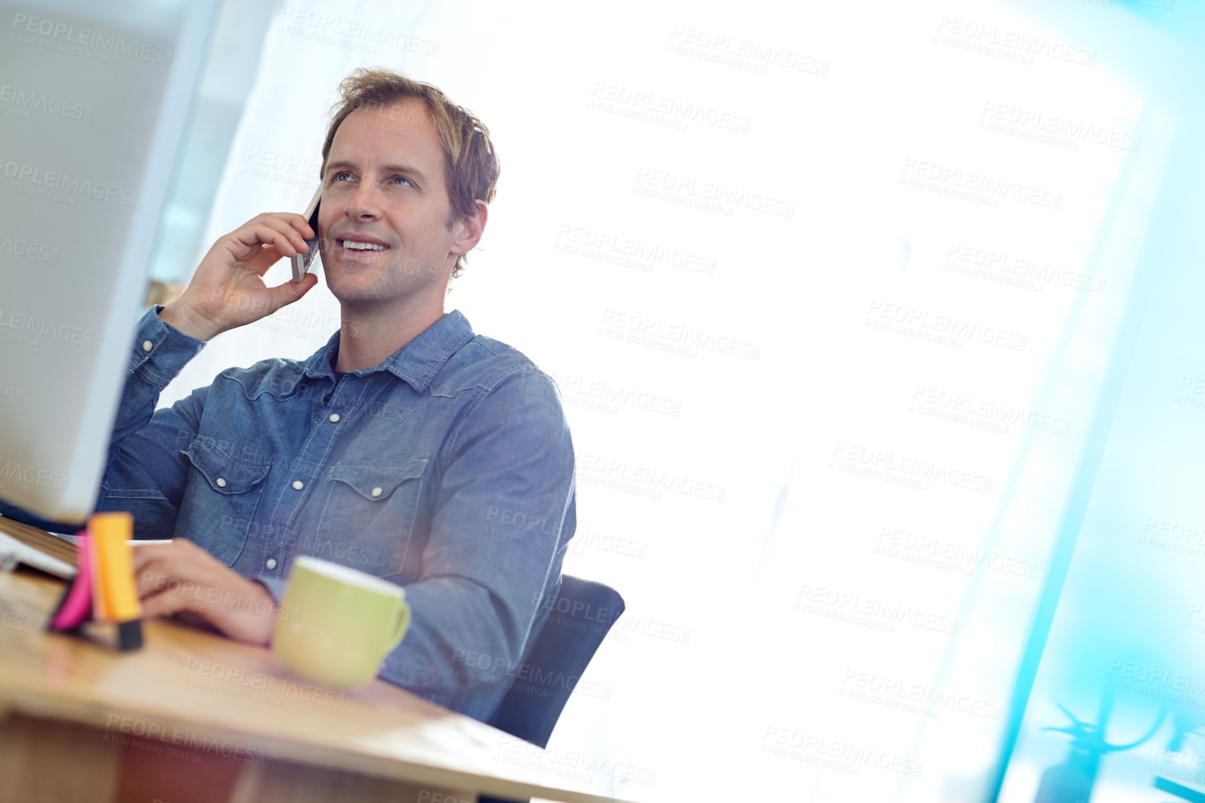 Buy stock photo Shot of a designer talking on a cellphone while working on a computer in an office