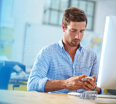 Buy stock photo Shot of a designer using a cellphone while working on a computer in an office