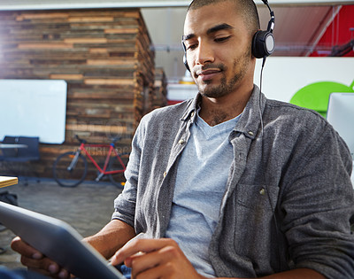 Buy stock photo Shot of a designer listening to music on a digital tablet in an office