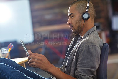 Buy stock photo Shot of a designer listening to music on a digital tablet in an office