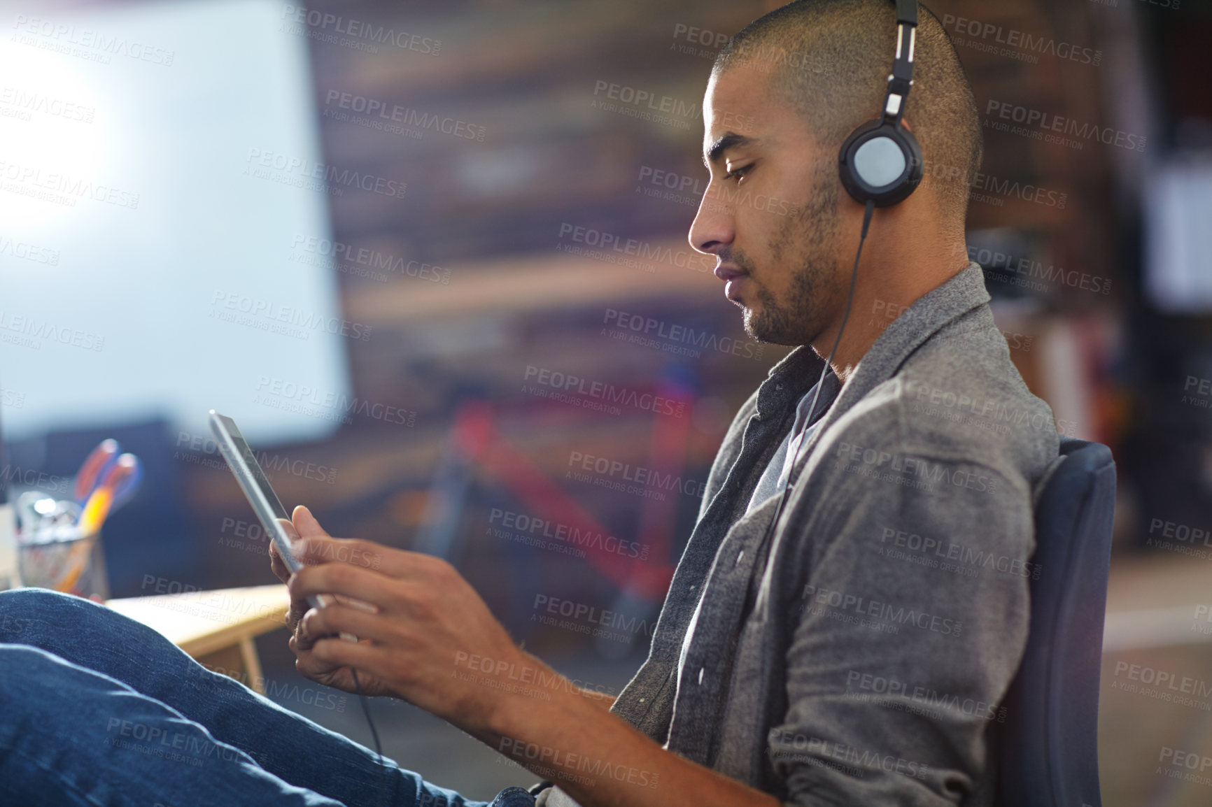 Buy stock photo Shot of a designer listening to music on a digital tablet in an office