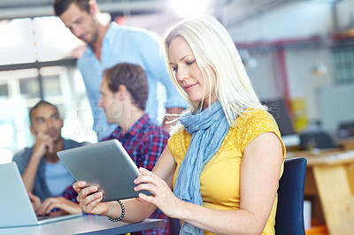 Buy stock photo Shot of a young designer using a digital tablet with colleagues in the background