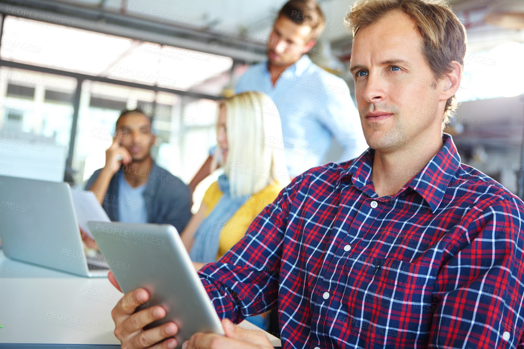 Buy stock photo Shot of a designer using a digital tablet with colleagues in the background