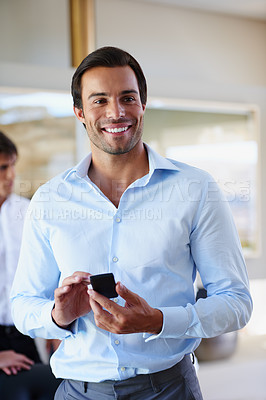 Buy stock photo Shot of a handsome businessman standing with his mobile phone at the office