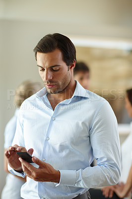 Buy stock photo Shot of a handsome businessman checking his mobile phone at the office