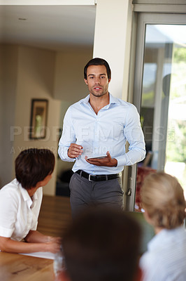 Buy stock photo Shot of a handsome businessman with a tablet delivering a presentation during a meeting