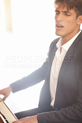 Buy stock photo Shot of a handsome young man singing while playing the piano